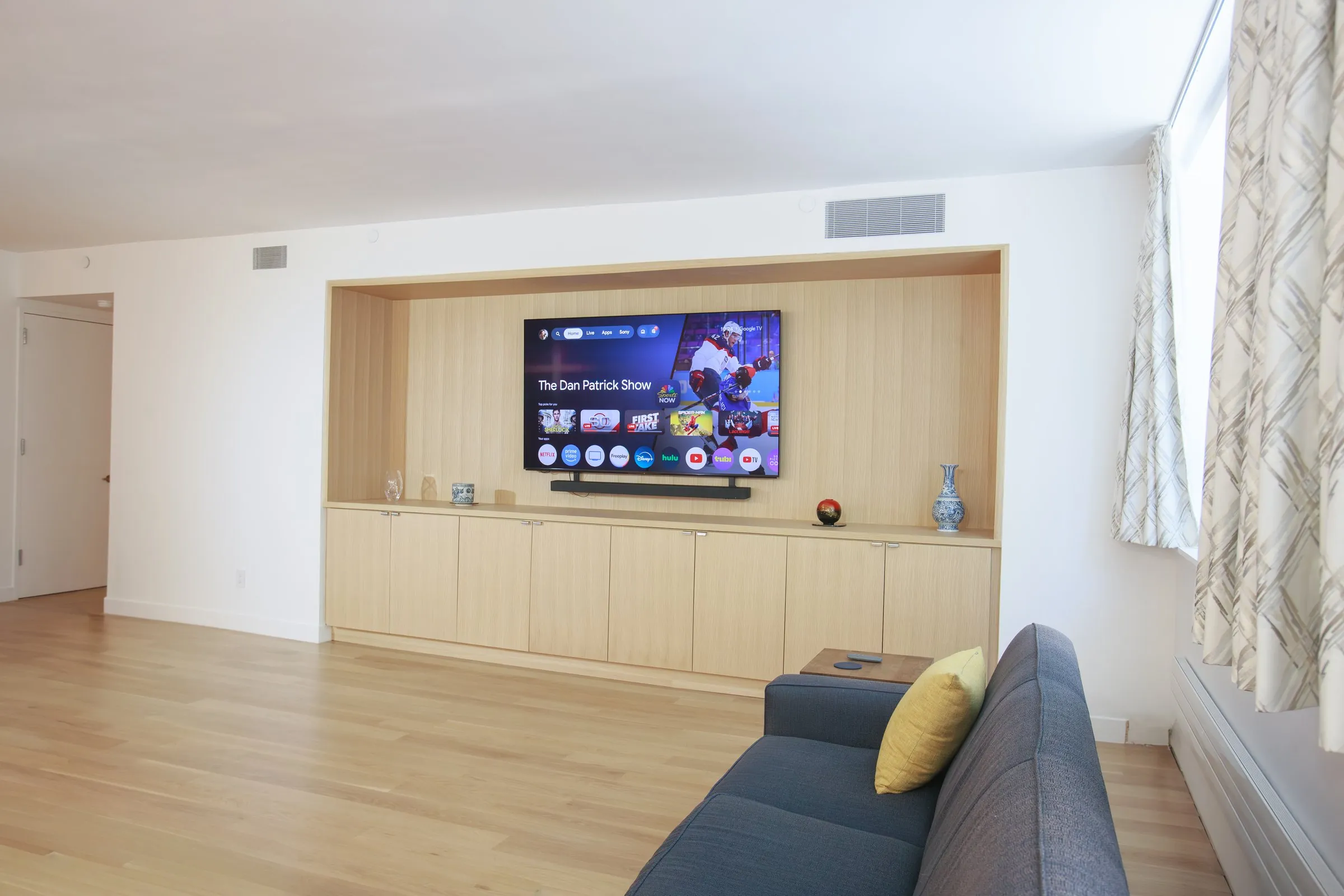 A bright minimalist NYC living room with a built-in oak media wall and large windows
