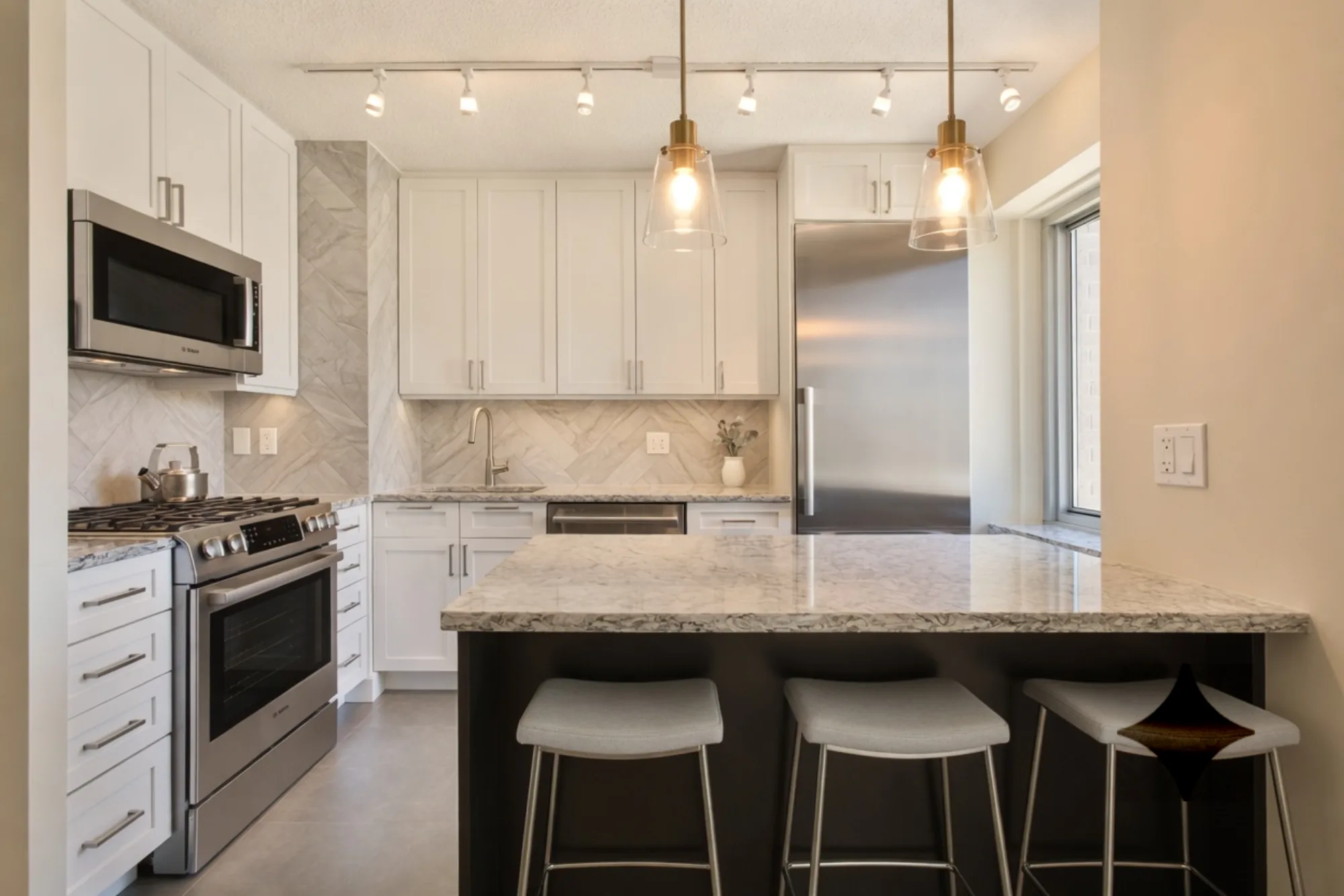 Custom white Shaker kitchen cabinetry with a herringbone marble backsplash
