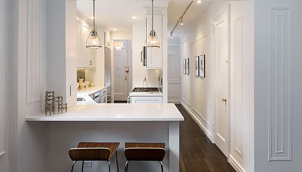 An elegant white peninsula kitchen with glass pendants and a quartz waterfall counter